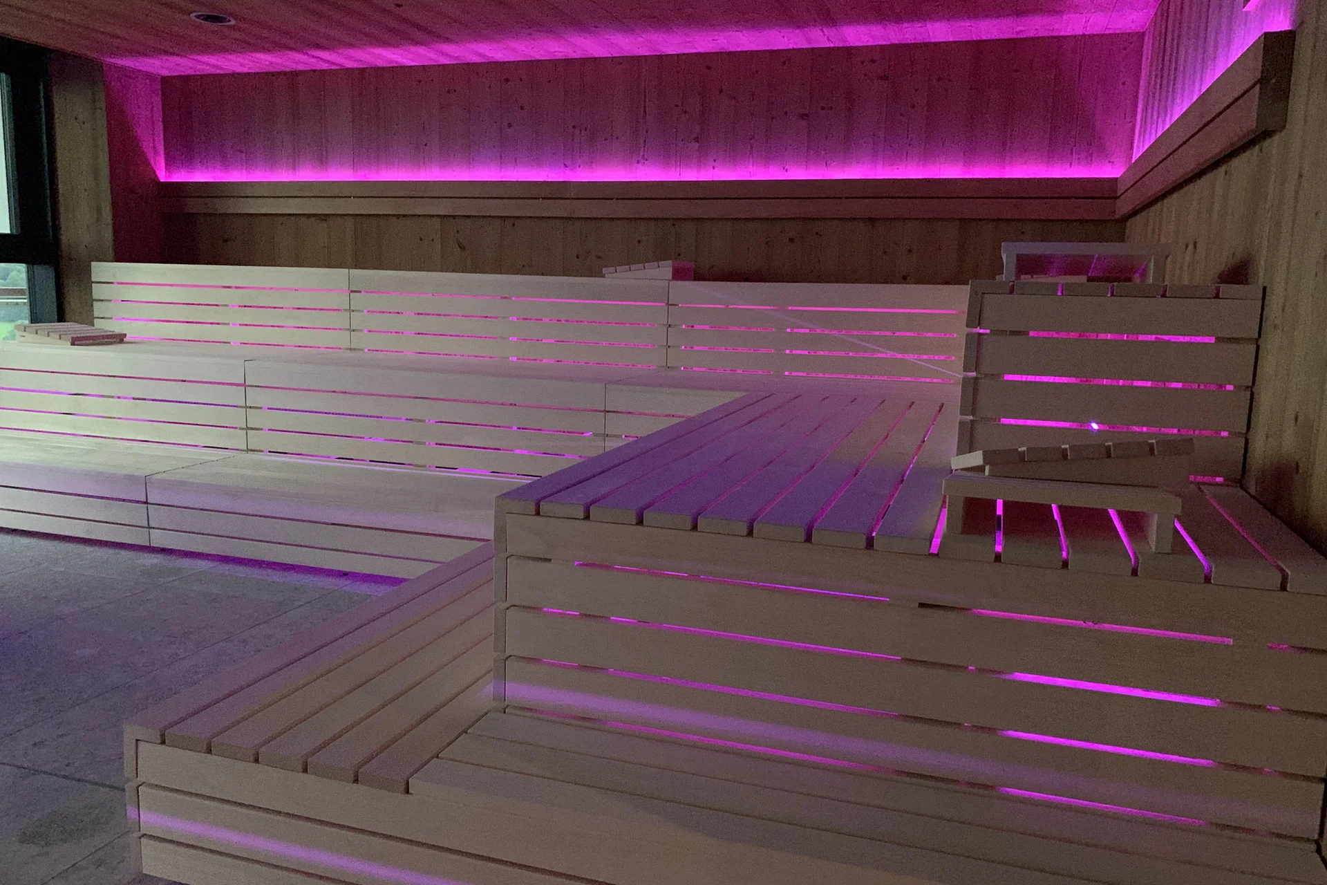 Innenraum einer Sauna mit lila LED-Beleuchtung und Holzbänken