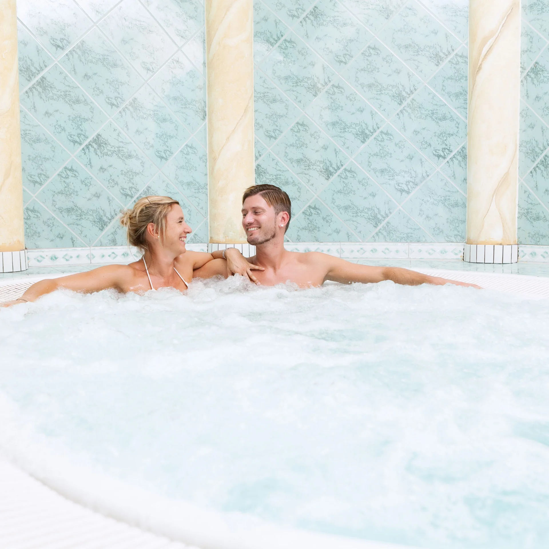 Paar entspannt im Whirlpool mit blauen Fliesen und Säulen