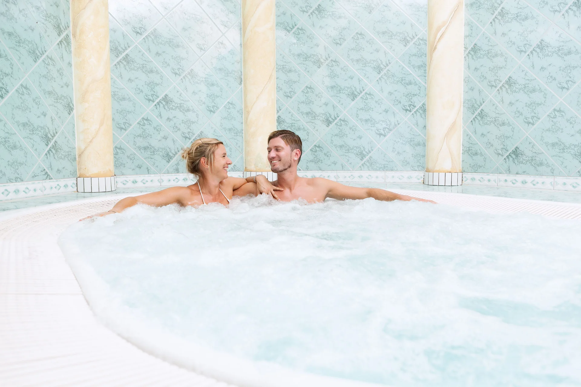 Paar entspannt im Whirlpool mit blauen Fliesen und Säulen
