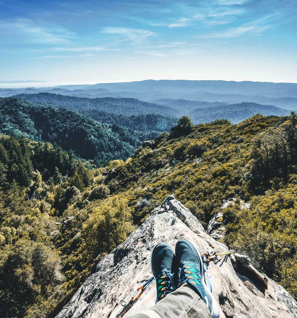 Wanderer mit blauen Schuhen sitzen auf Felsen mit Blick auf bewaldete Berge