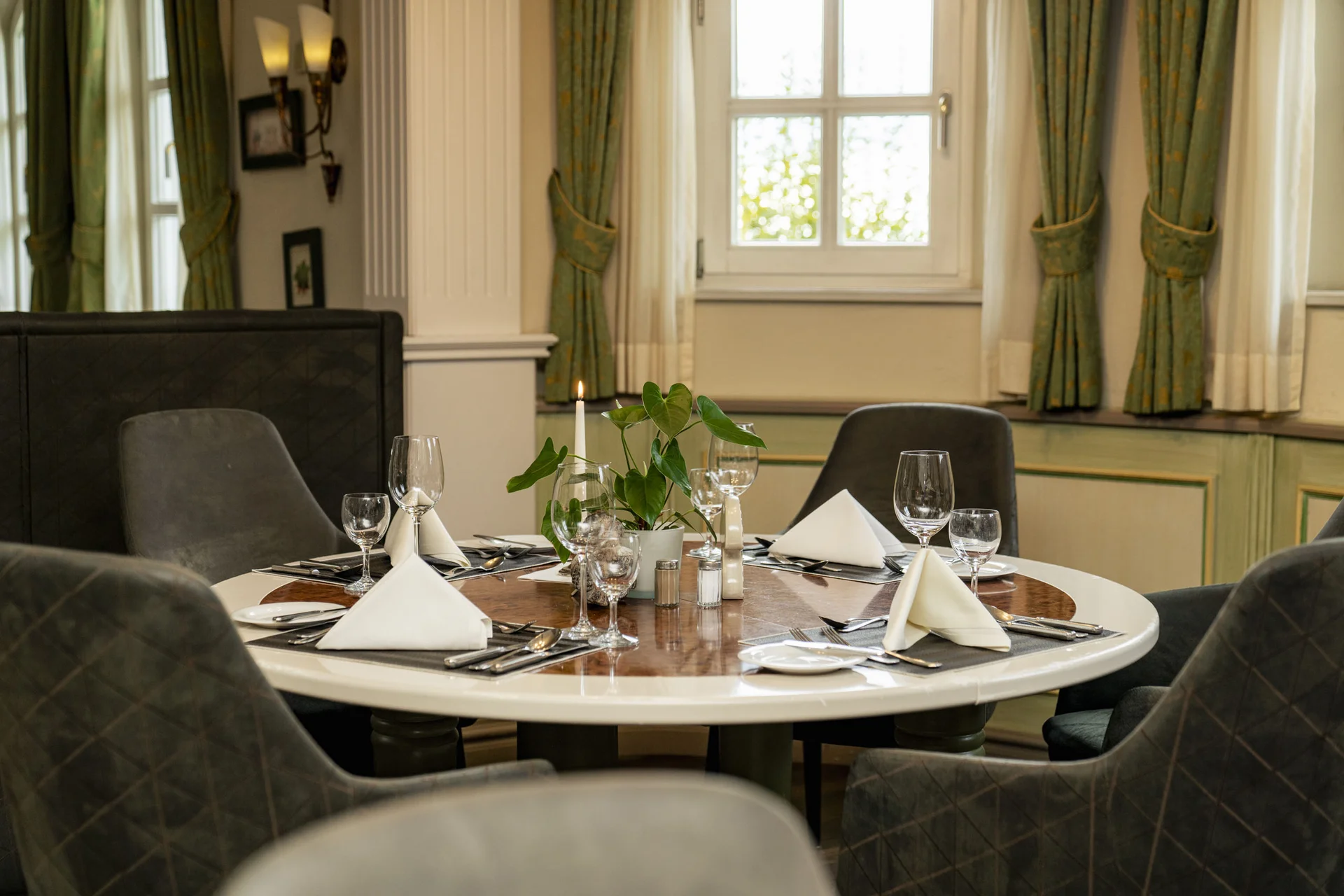 Eleganter gedeckter runder Tisch in einem Restaurant mit grün-goldenen Vorhängen
