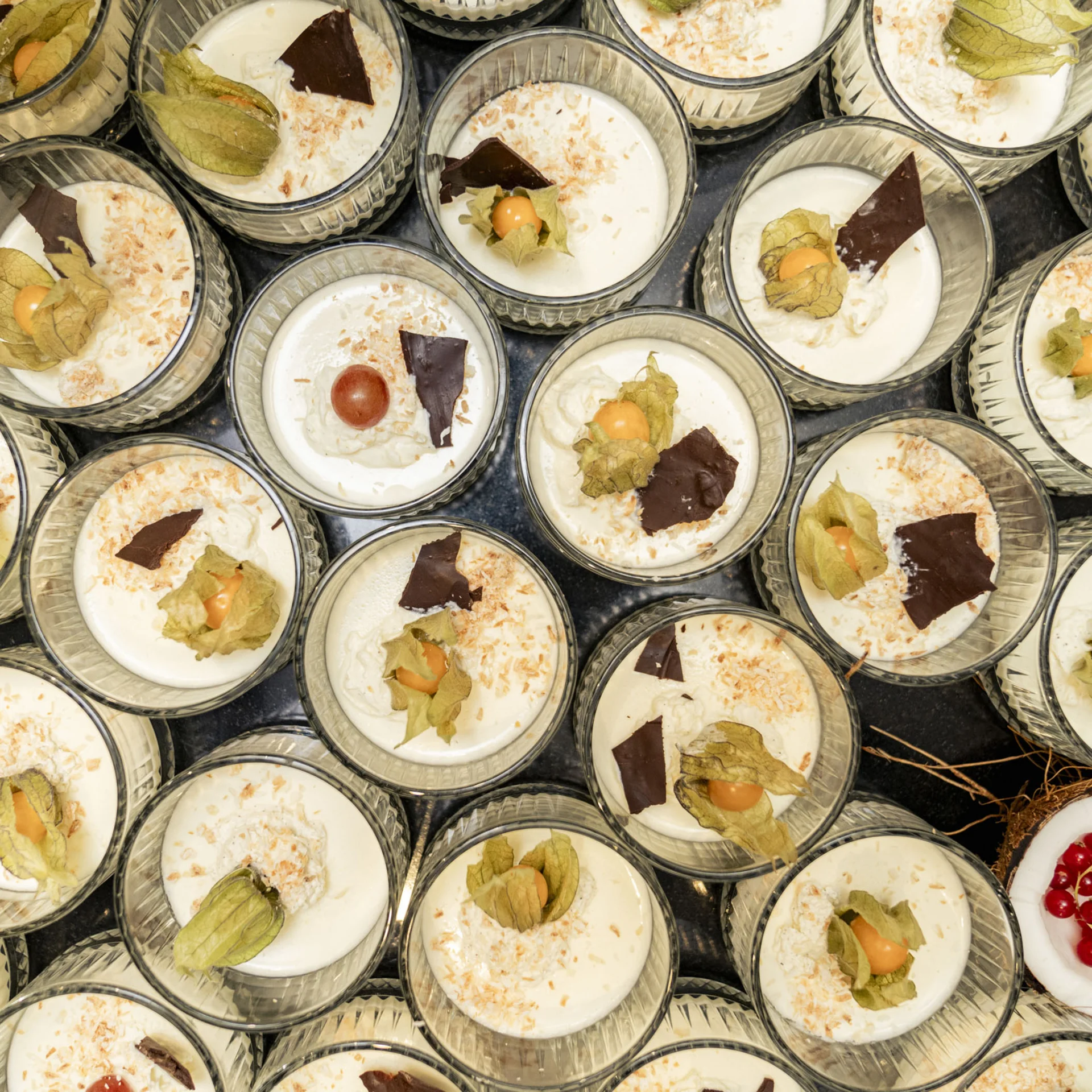Mehrere Gläser mit weißem Dessert, dekoriert mit Früchten und Schokolade