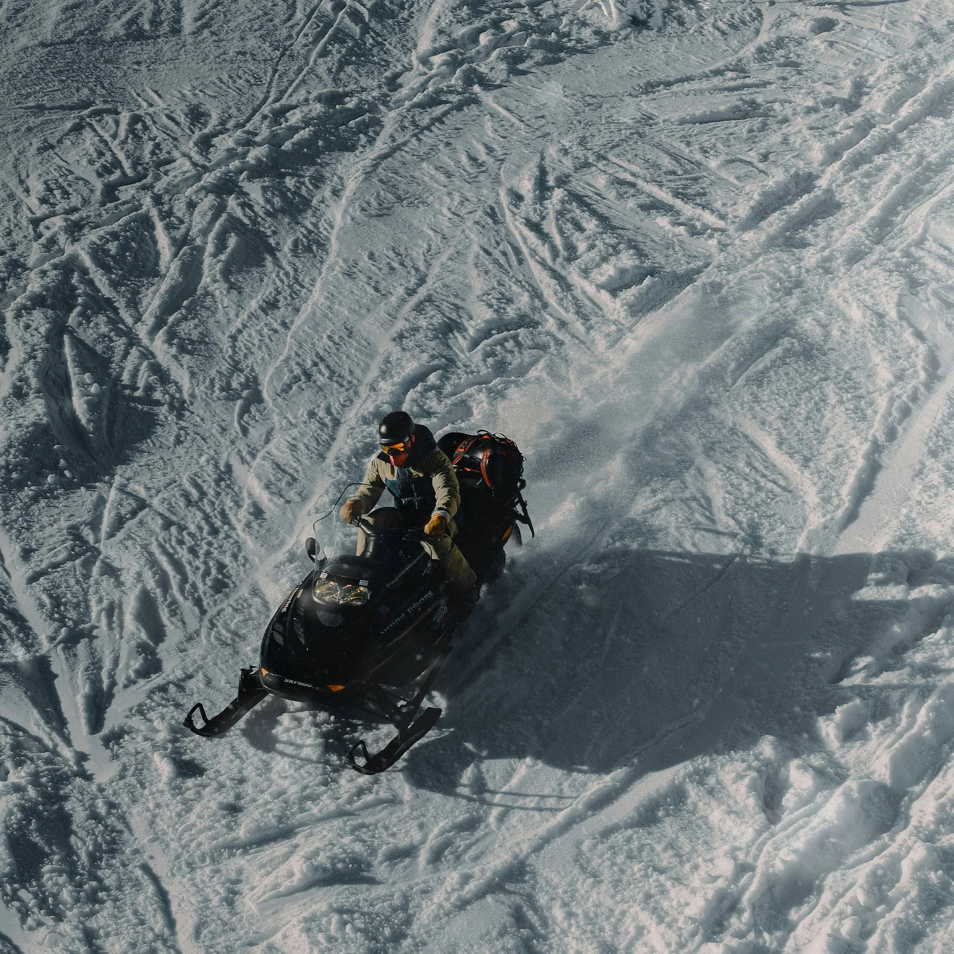 Zwei Personen fahren mit einem Schneemobil auf verschneitem Gelände
