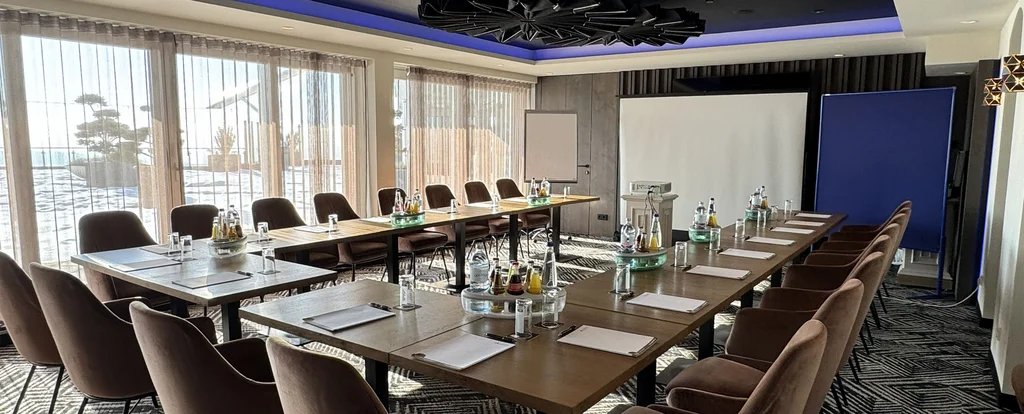 Konferenzraum mit U-förmigem Tisch, Stühlen und Projektionsleinwand