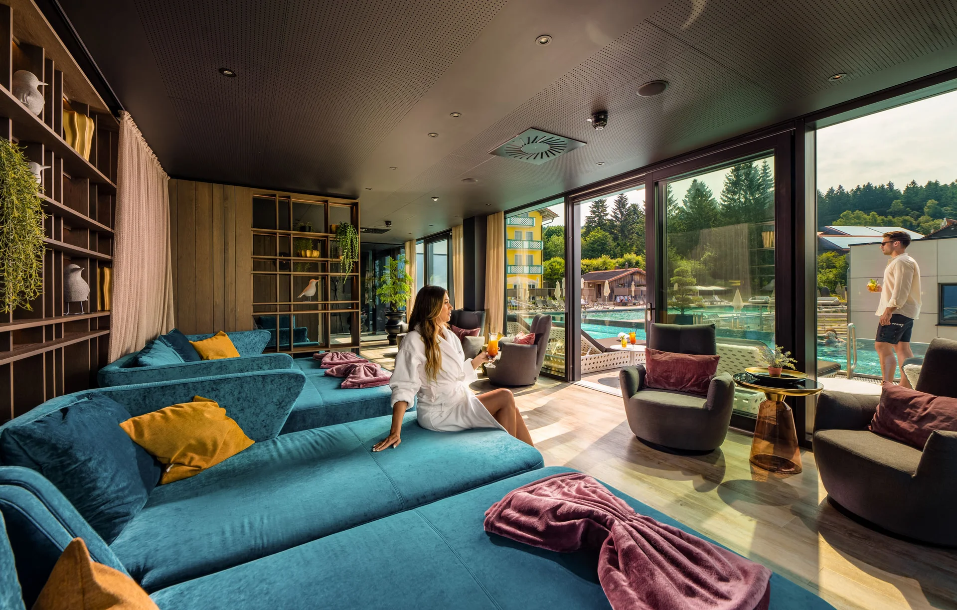 Frau entspannt im Bademantel in Lounge mit Blick auf Pool und Terrasse