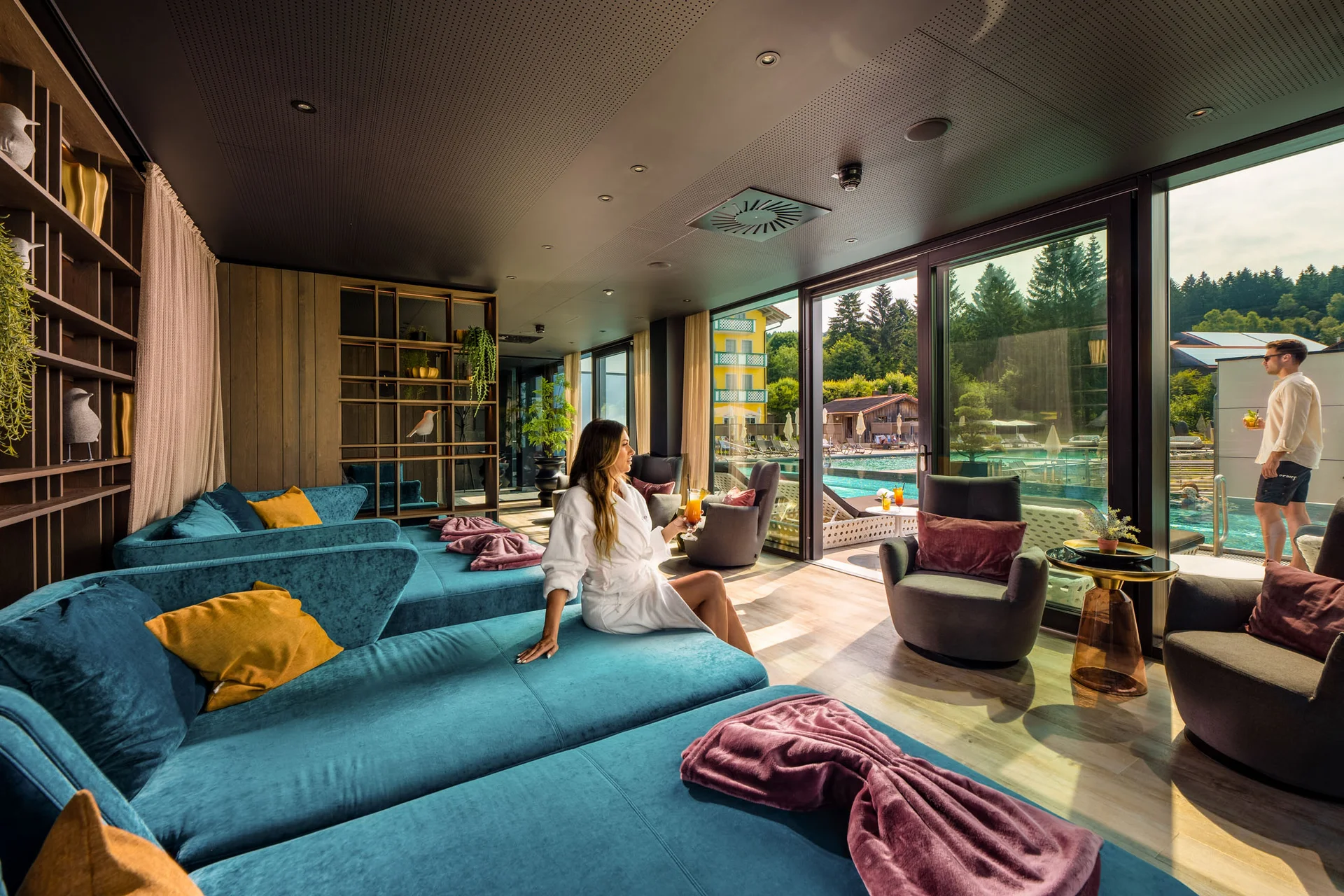 Frau entspannt im Bademantel in Lounge mit Blick auf Pool und Terrasse