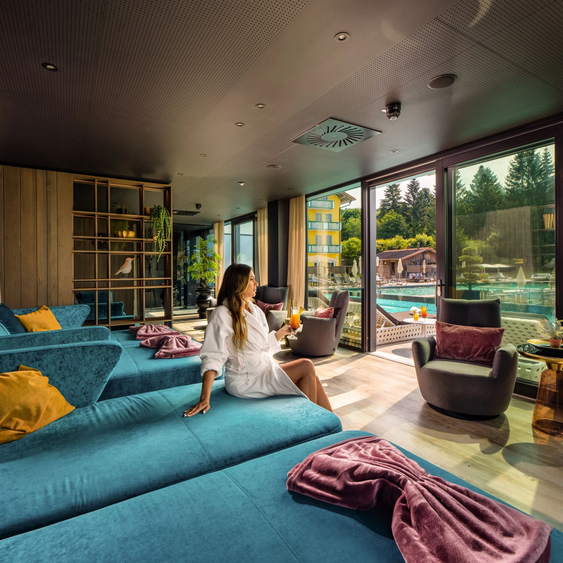 Frau entspannt im Bademantel in Lounge mit Blick auf Pool und Terrasse