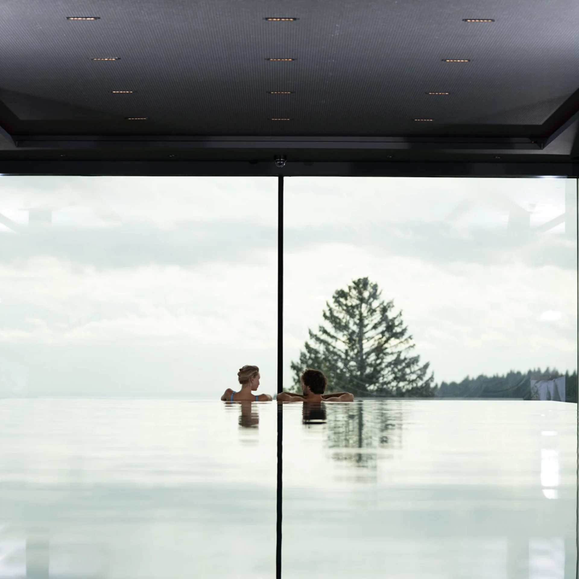 Paar entspannt im Infinity-Pool mit Glasfront und Bergsicht