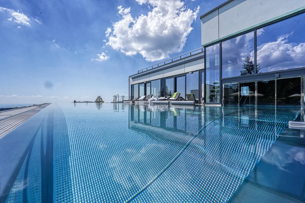 Für Feiern in kleiner und großer Runde Moderner Glasbau mit Infinitypool und Liegen unter blauem Himmel
