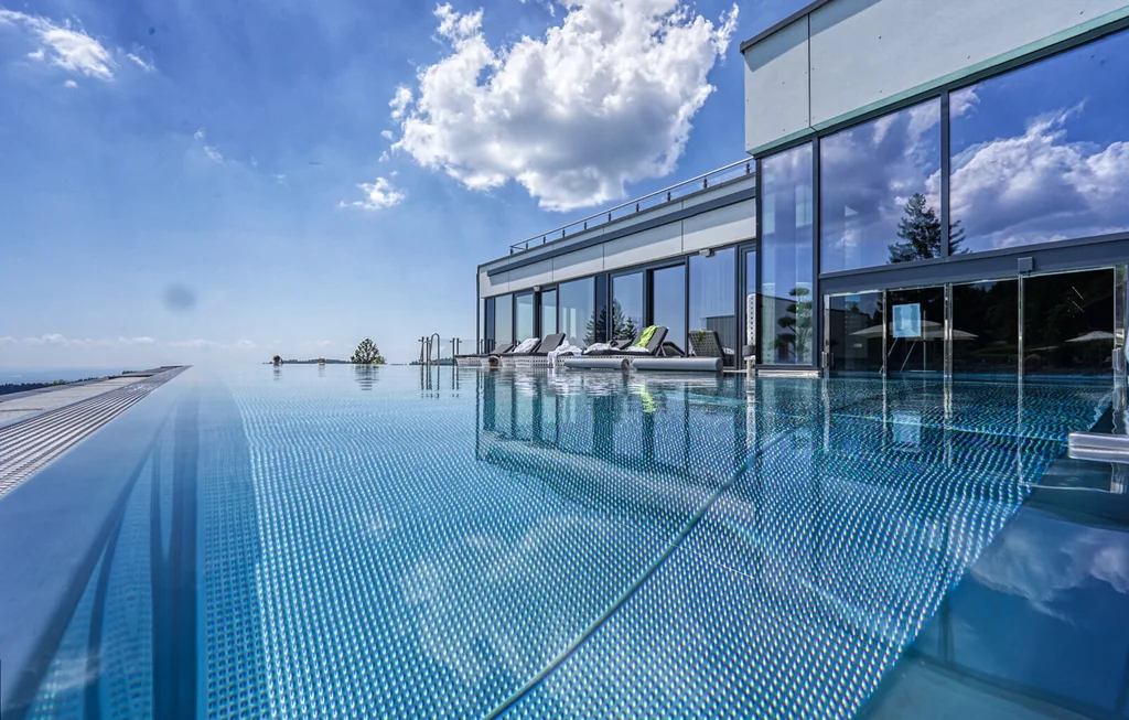 Für Feiern in kleiner und großer Runde Moderner Glasbau mit Infinitypool und Liegen unter blauem Himmel