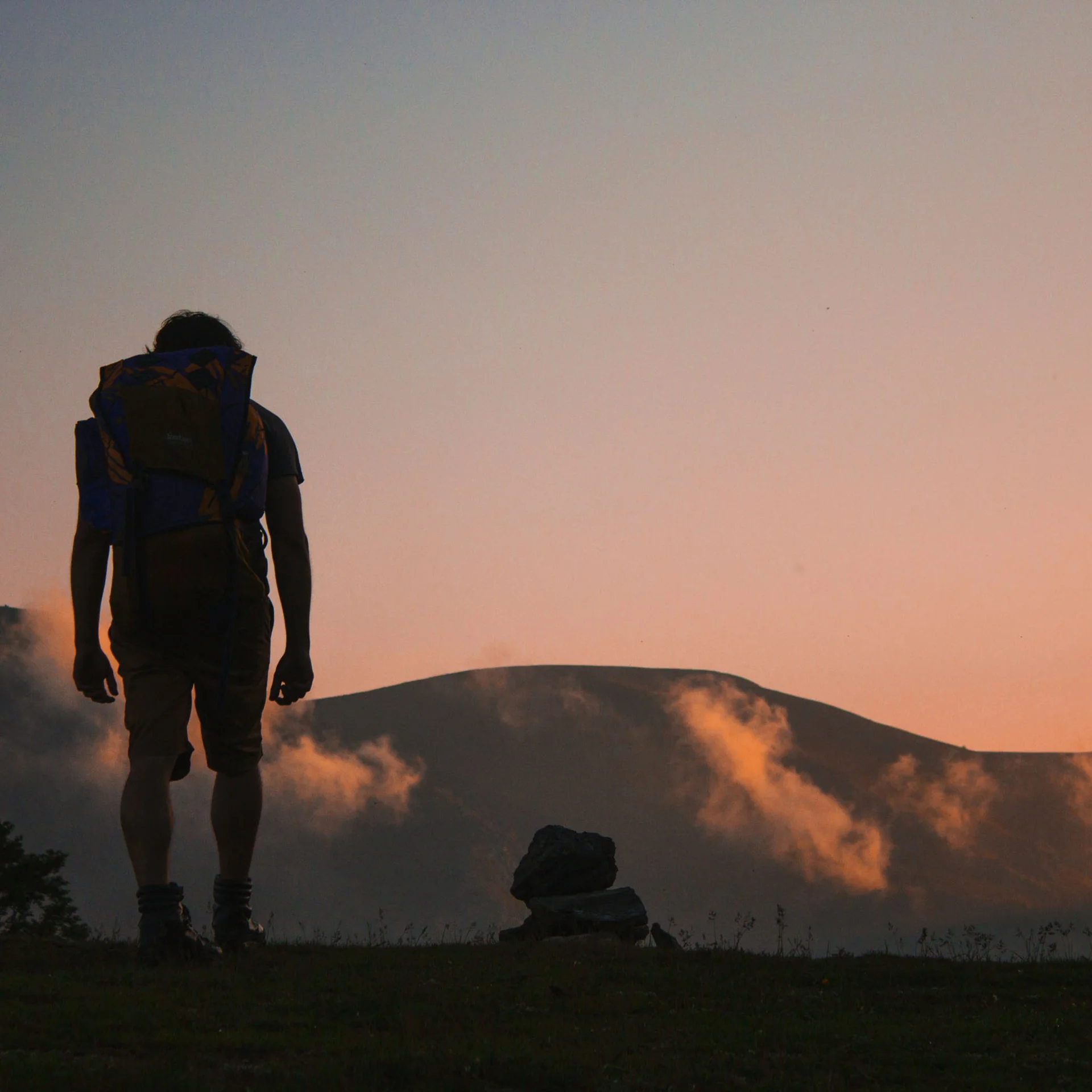 Person mit Rucksack vor Berg bei Sonnenuntergang