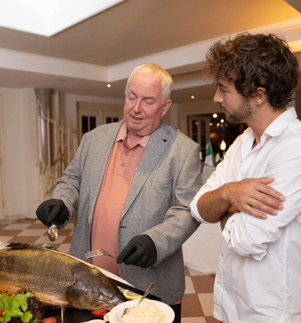 Älterer Mann erklärt junger Mann Zubereitung eines großen Fisches im Restaurant