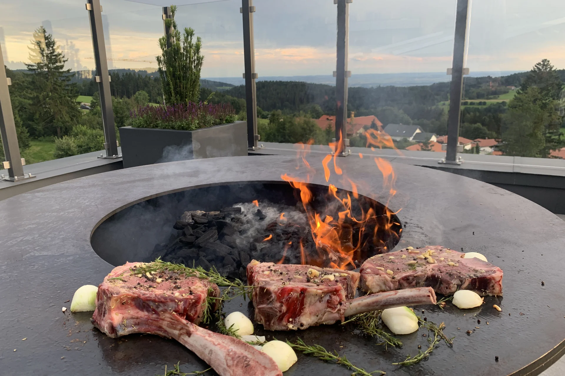Fleischstücke und Gemüse auf Grillplatte mit offener Flamme und Bergblick