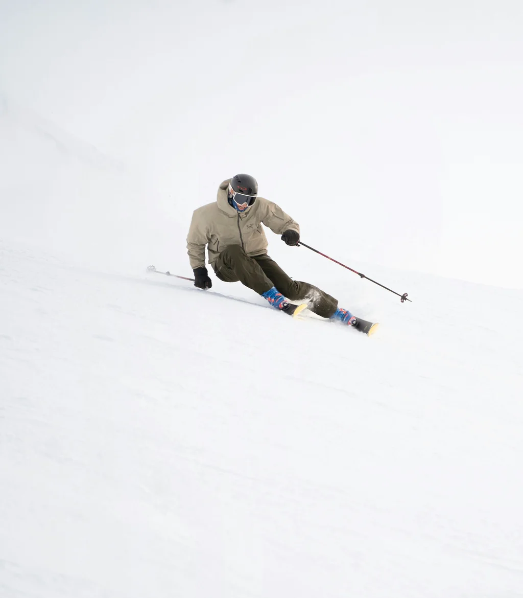 Skifahrer in brauner Jacke fährt auf verschneiter Piste bei Nebel