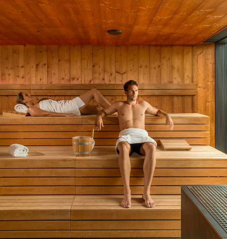 Mann und Frau entspannen in einer modernen Sauna mit Holzwänden und großen Fenstern