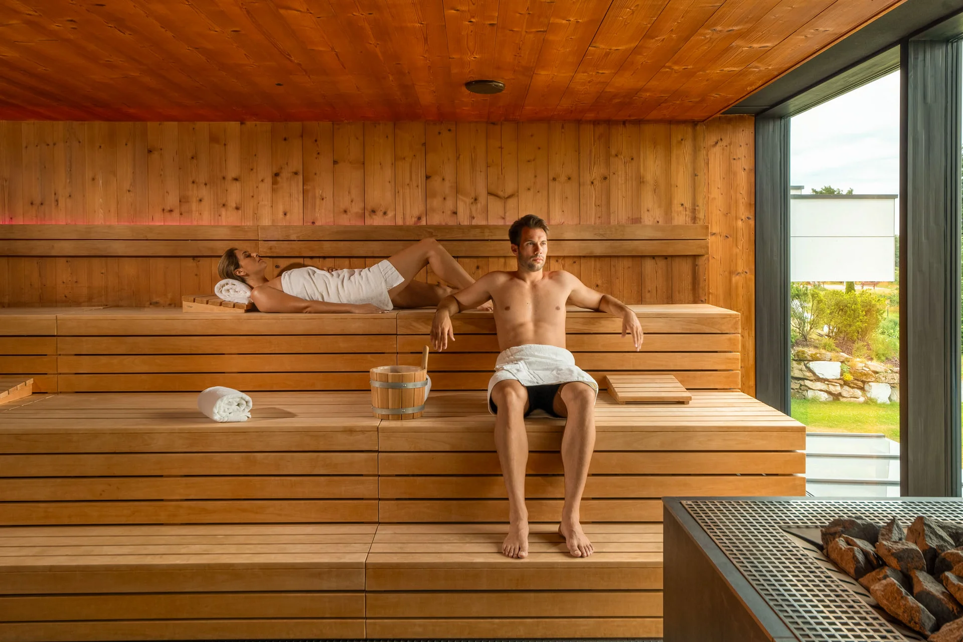 Mann und Frau entspannen in einer modernen Sauna mit Holzwänden und großen Fenstern