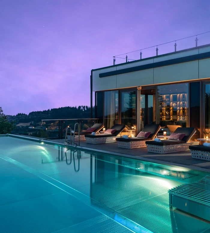 Beleuchteter Pool auf einer Dachterrasse mit Liegen und Blick auf die Hügellandschaft in der Dämmerung