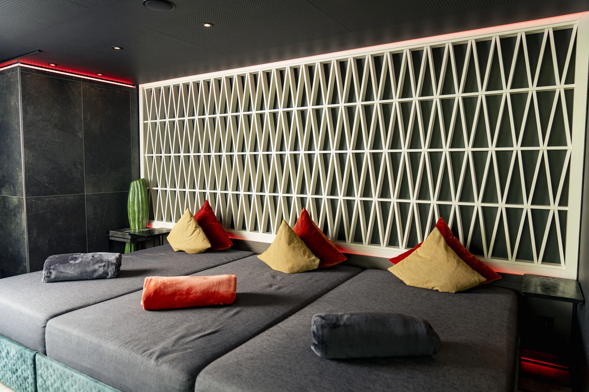 Moderne Lounge mit grauen Sofas und bunten Kissen vor einem geometrisch gefliesten Wandpaneel