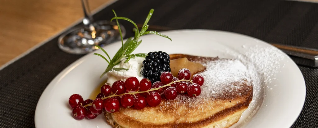 Die Adresse für Wellness in Bayern: Ihr Hotel in St. Englmar Pfannkuchen mit Beeren und Sahne auf weißem Teller mit Glas Saft