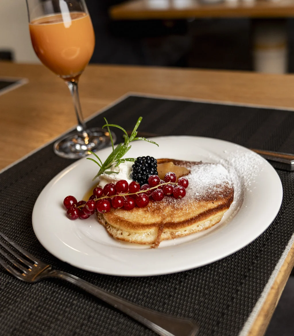 Pfannkuchen mit Beeren und Sahne auf weißem Teller mit Glas Saft