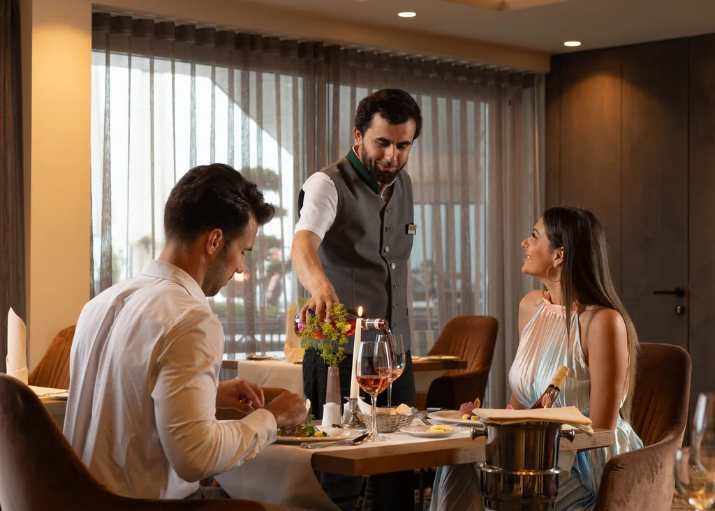 Die Adresse für Wellness in Bayern: Ihr Hotel in St. Englmar Kellner serviert Gästen Wein im eleganten Restaurant