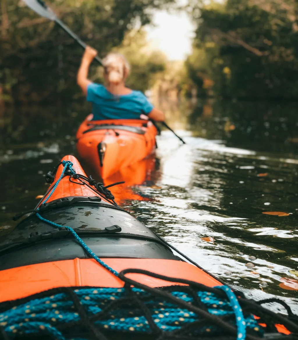 Person paddelt in einem orangefarbenen Kajak auf einem ruhigen Fluss