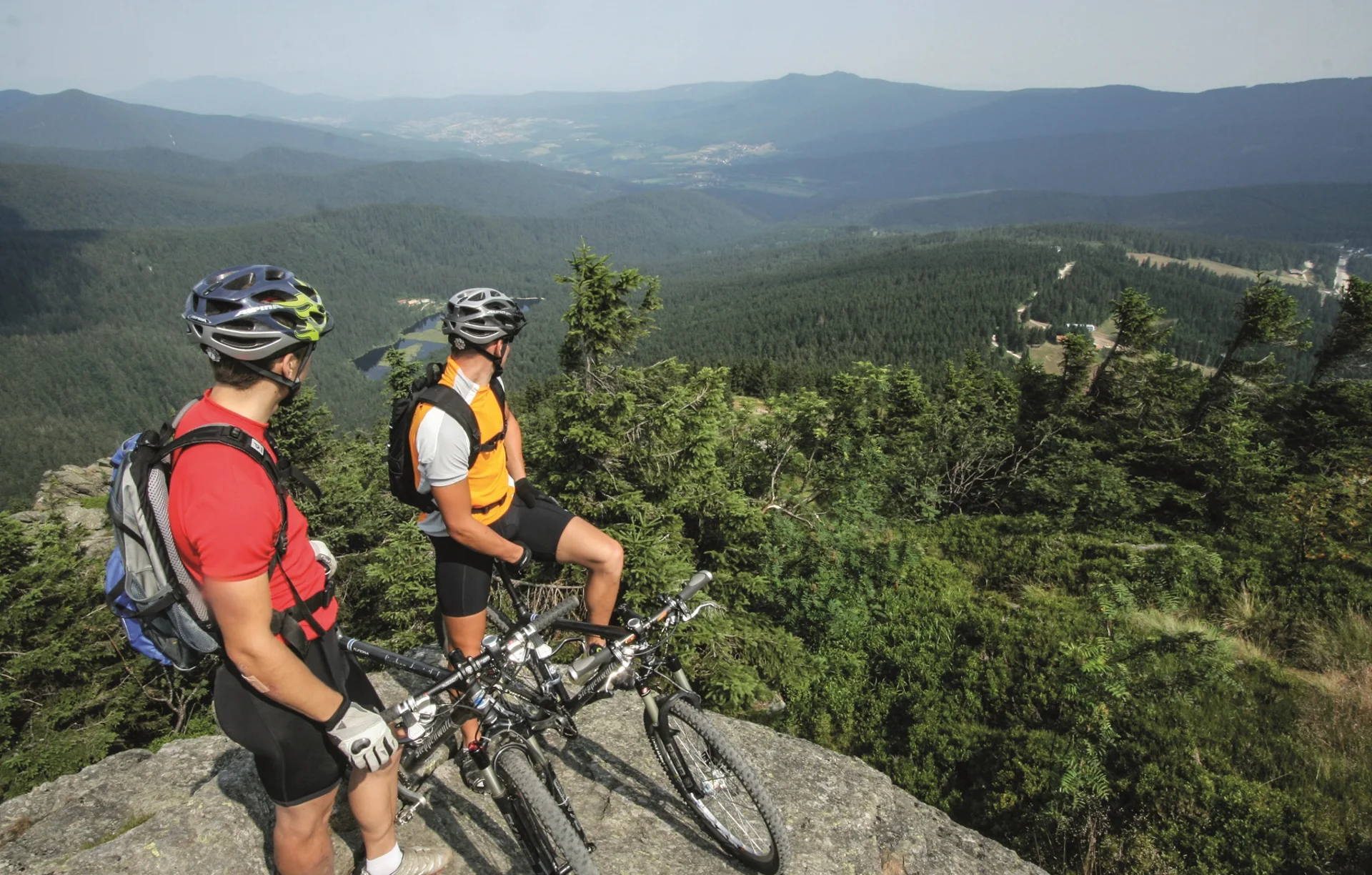 Zwei Mountainbiker mit Helm blicken auf bewaldete Berge und Tal