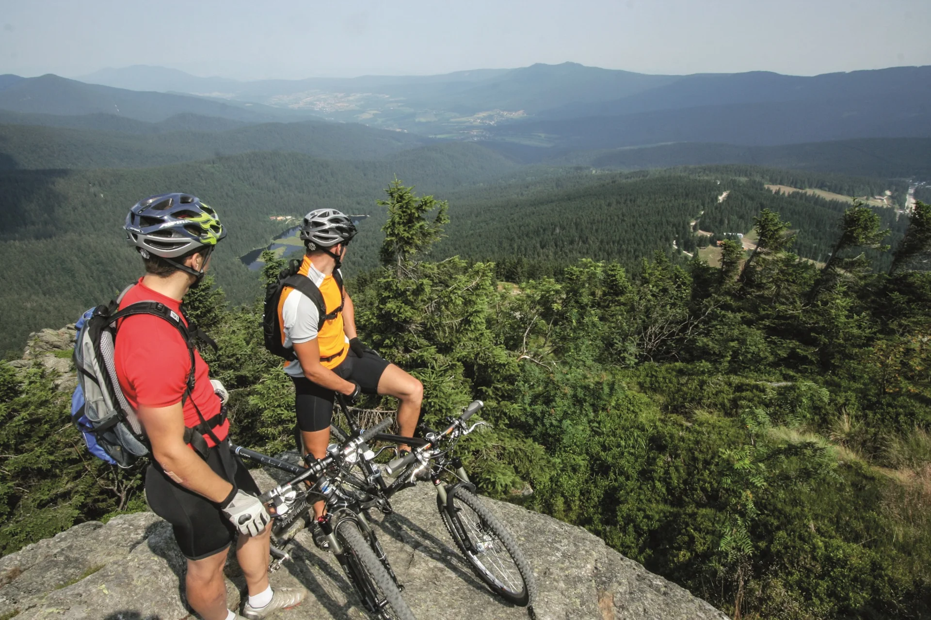 Zwei Mountainbiker mit Helm blicken auf bewaldete Berge und Tal