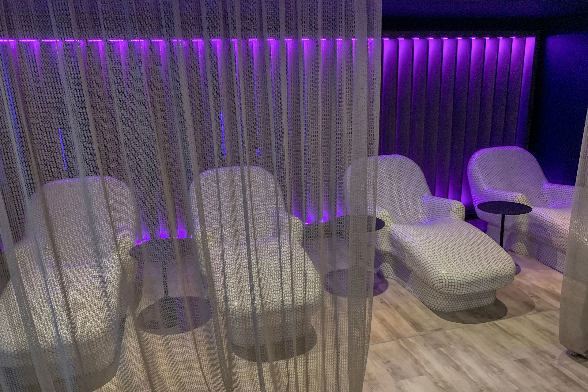 Moderne Lounge mit weißen Sesseln und lila Beleuchtung hinter einem Netzvorhang