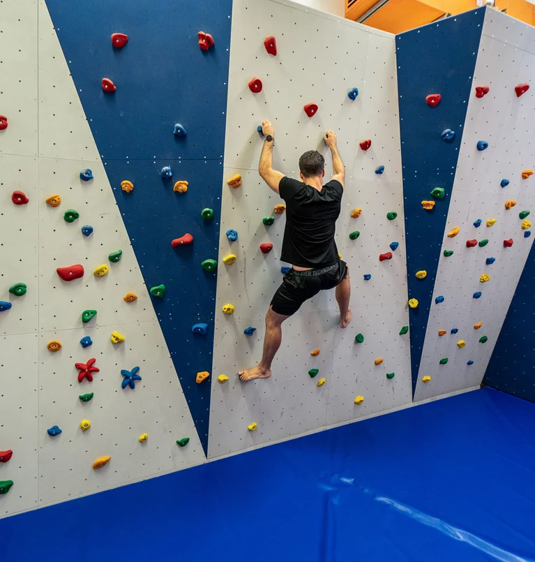 Mann klettert an einer bunten Indoor-Kletterwand mit blauem Boden