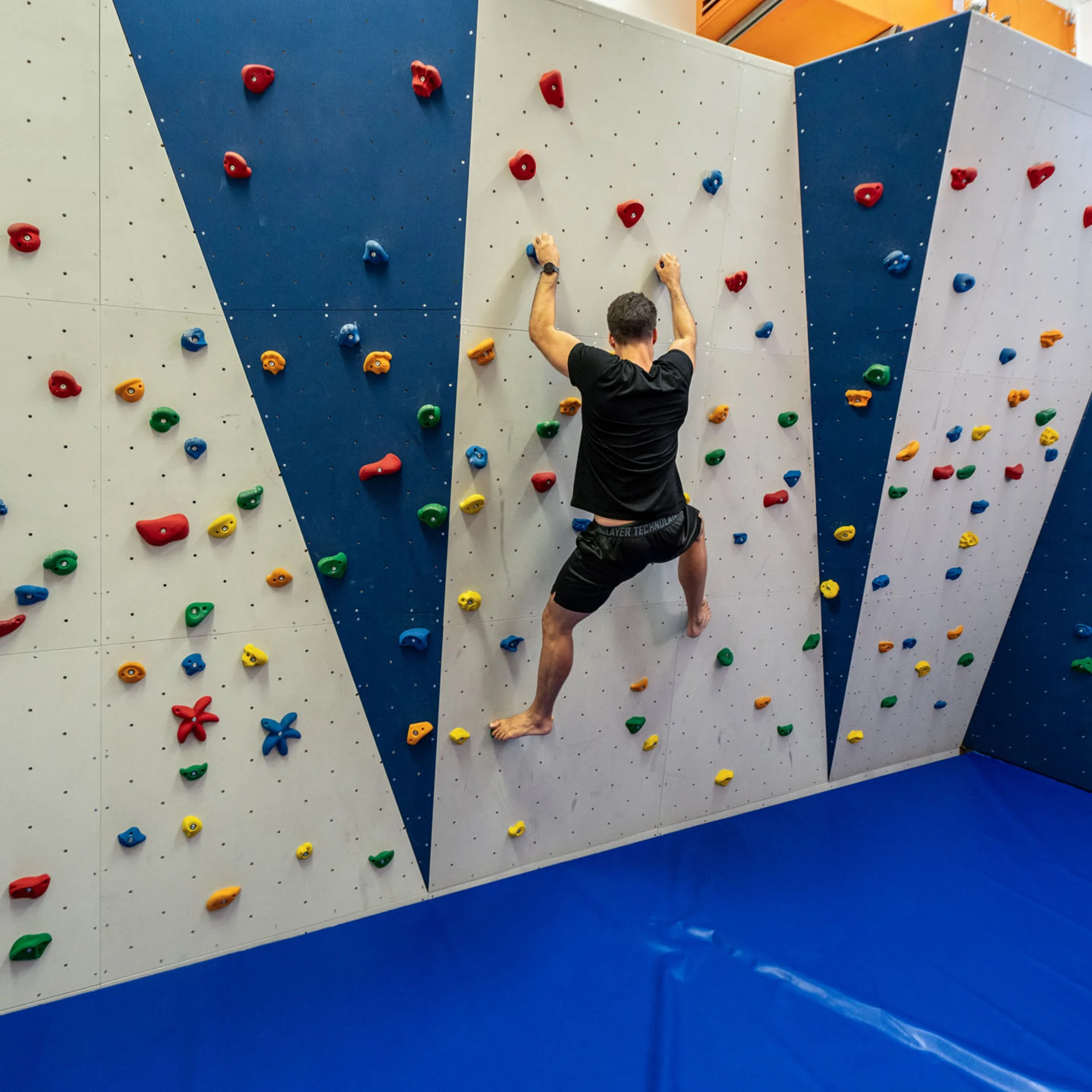Mann klettert an einer bunten Indoor-Kletterwand mit blauem Boden