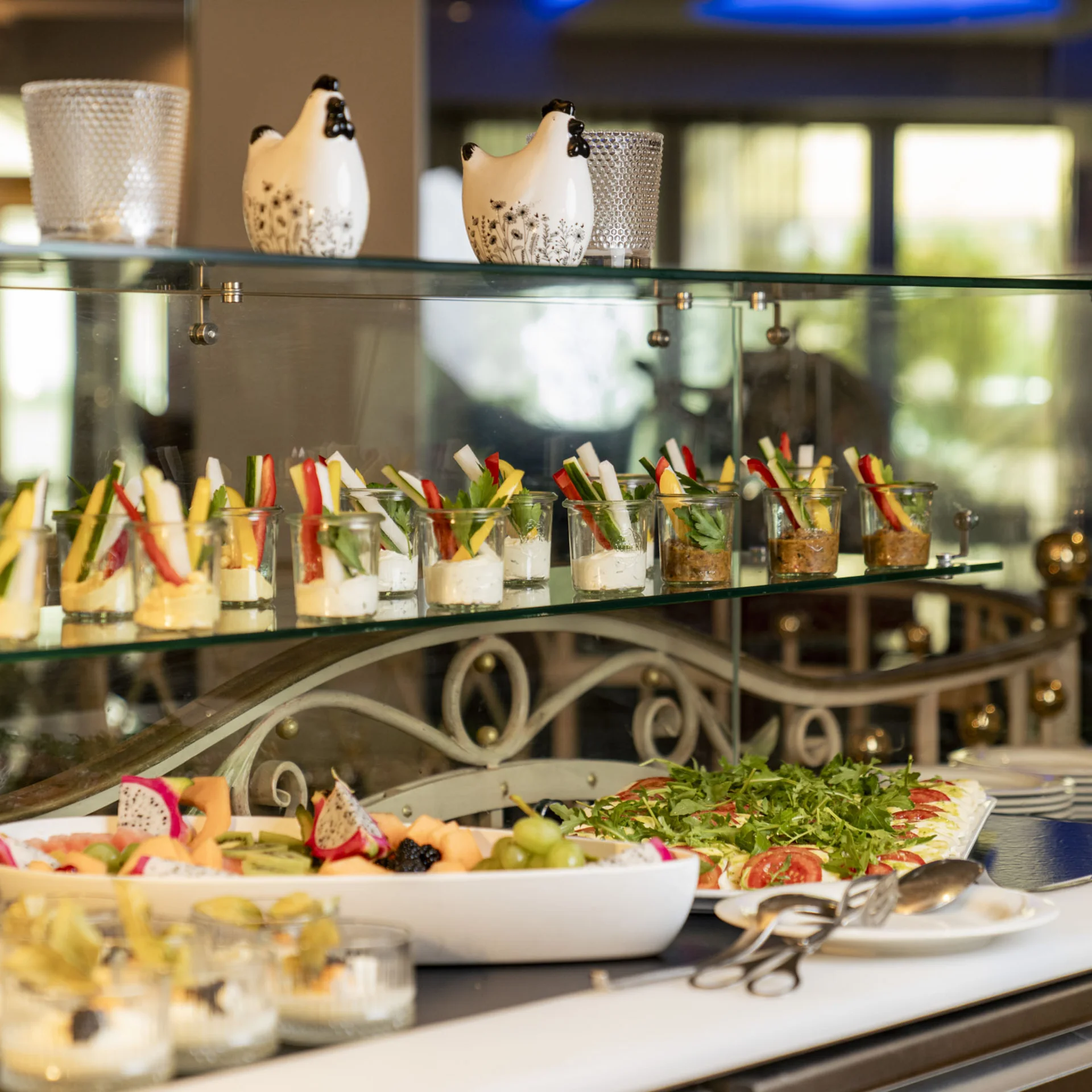 Buffet mit kleinen Gläsern gefüllt mit Gemüse und Dip, Obst und Salat auf Teller