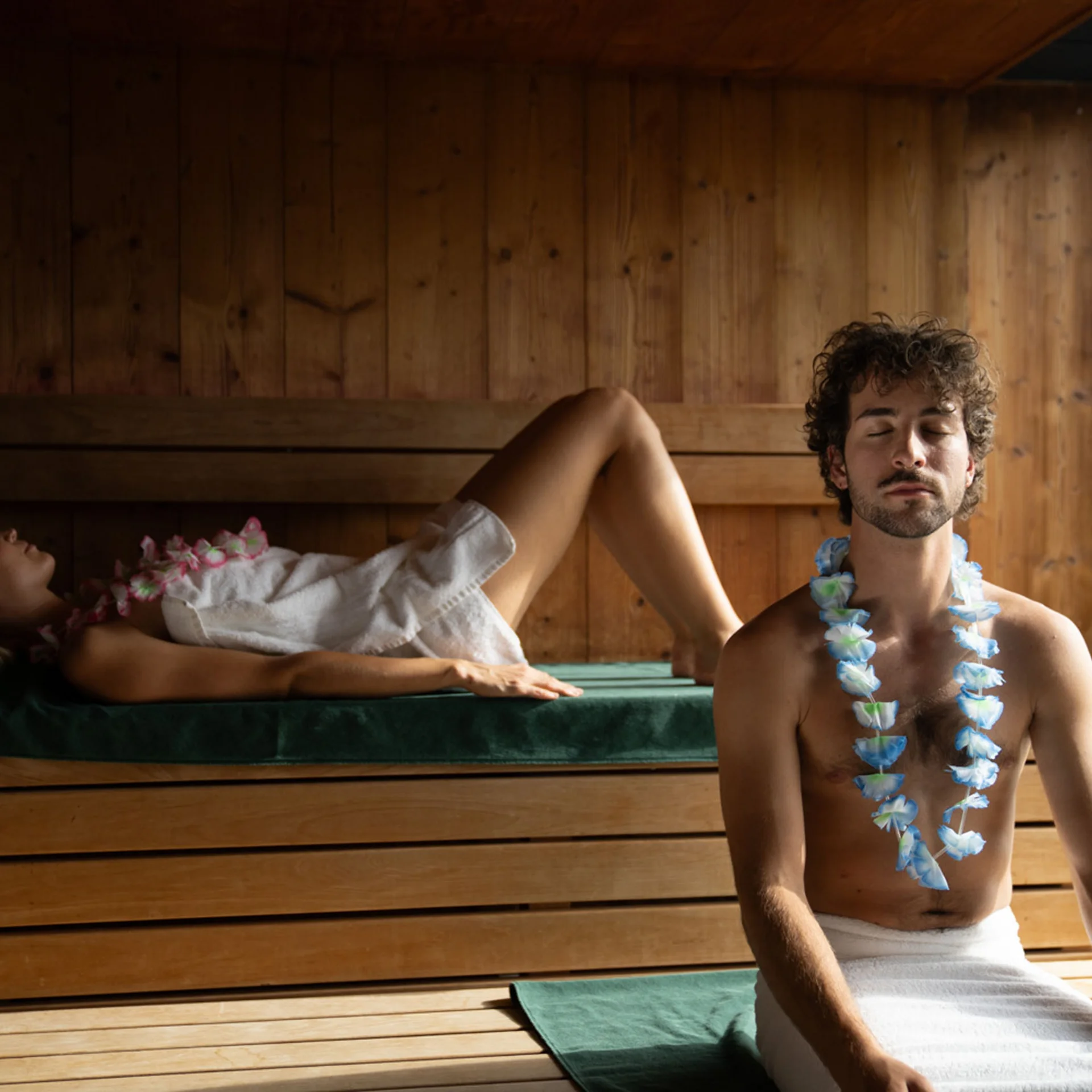 Zwei Menschen entspannen in einer Holzsauna mit Blumenketten