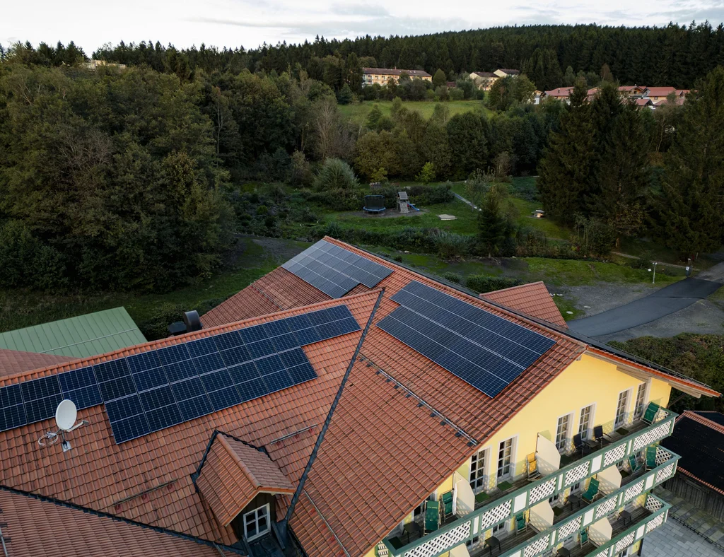 Dach mit Solarpanelen vor Wald und Dorf im Hintergrund