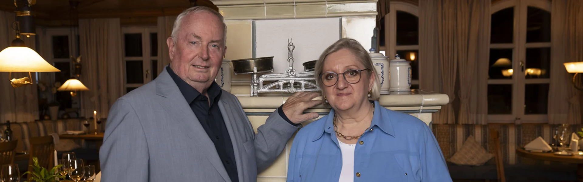 Älteres Paar steht vor einem traditionellen weißen Kachelofen in einem Restaurant