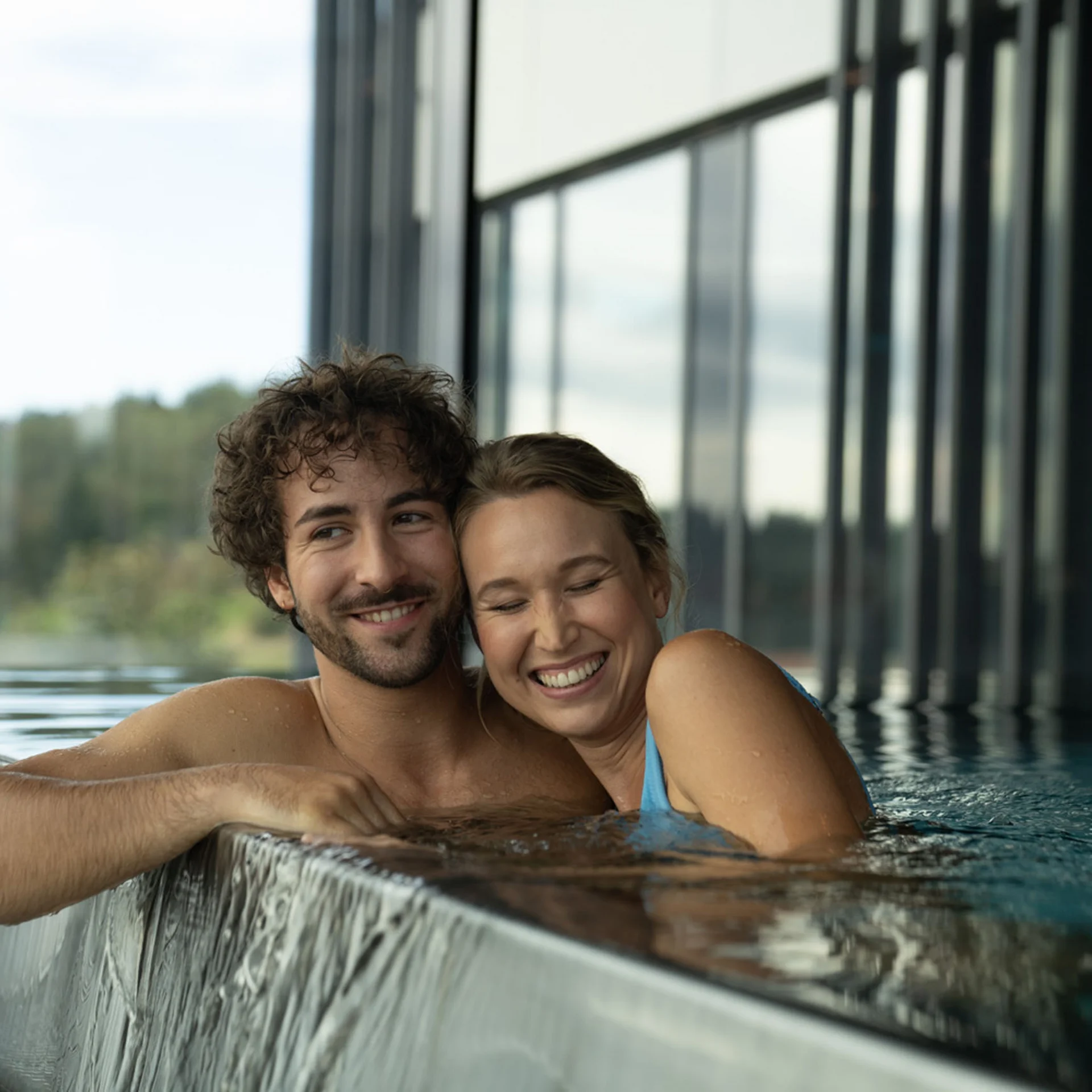Lächelndes Paar entspannt im Indoor-Pool an Wasserfallkante