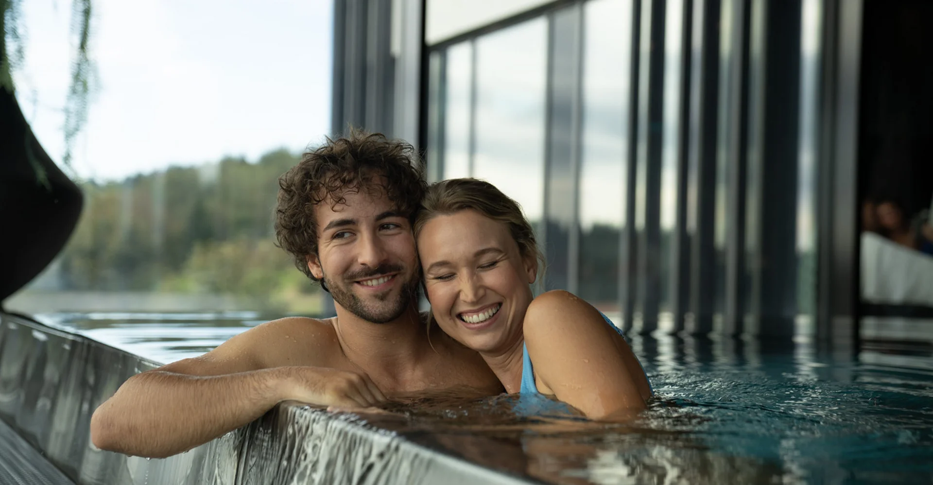 Lächelndes Paar entspannt im Indoor-Pool an Wasserfallkante