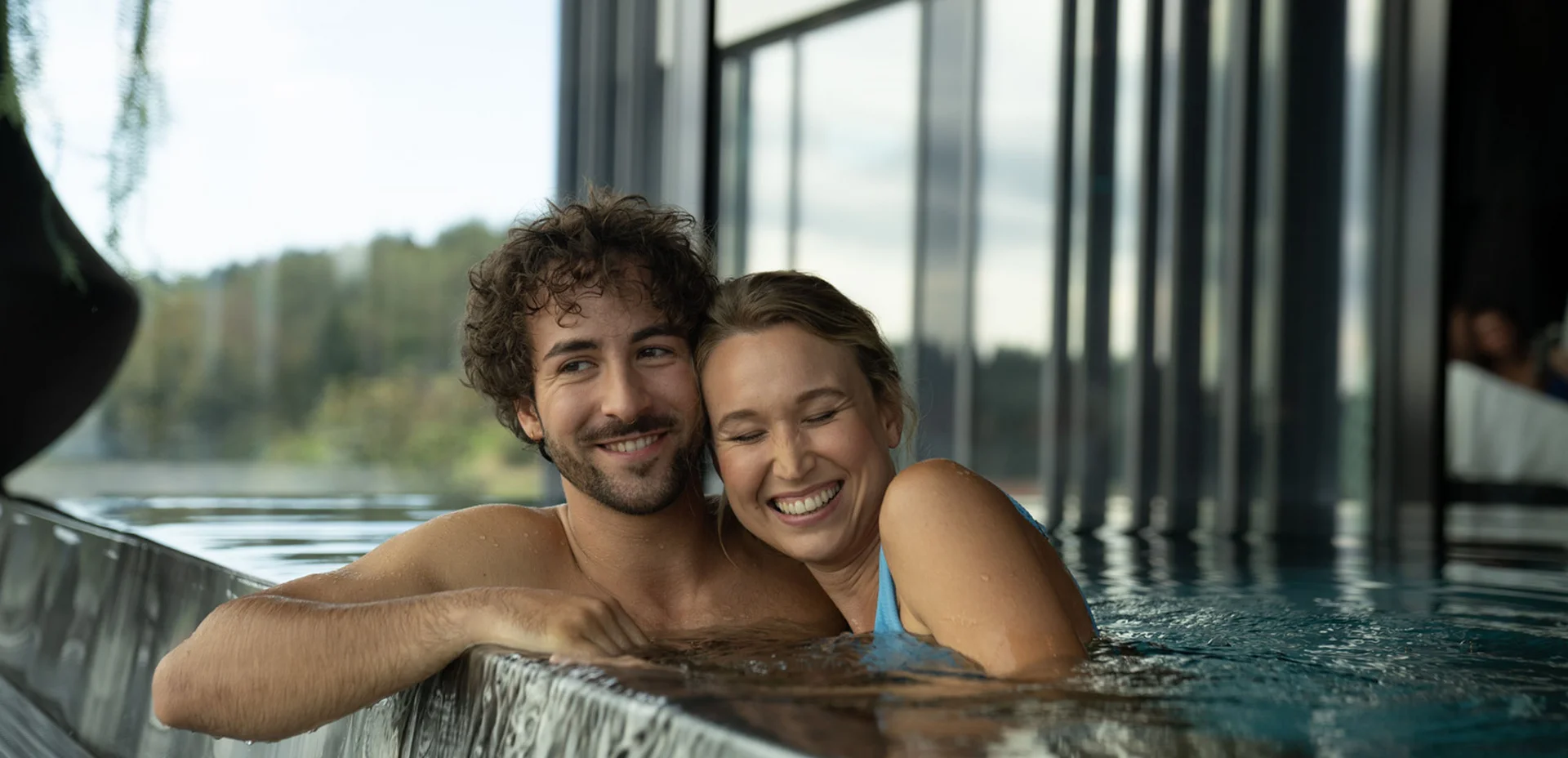 Lächelndes Paar entspannt im Indoor-Pool an Wasserfallkante