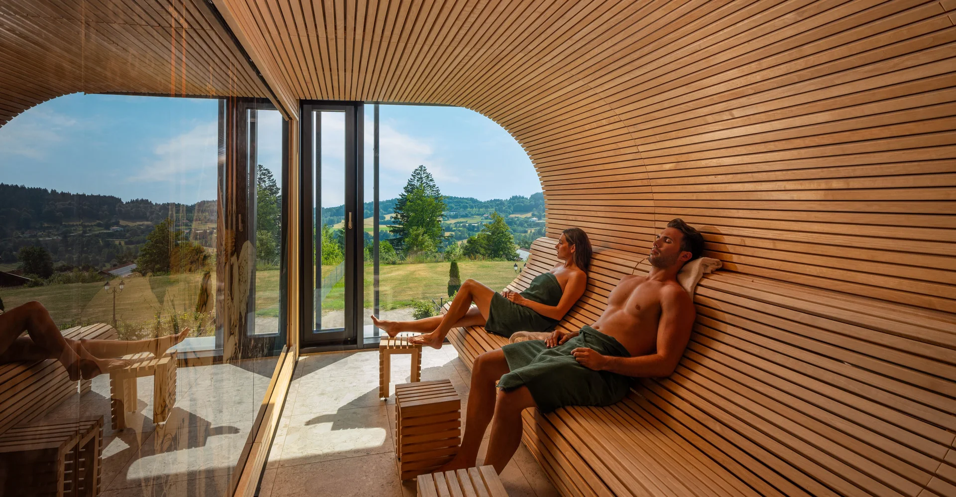 Zwei Personen entspannen in einer Sauna mit Fenster und Blick auf die Landschaft