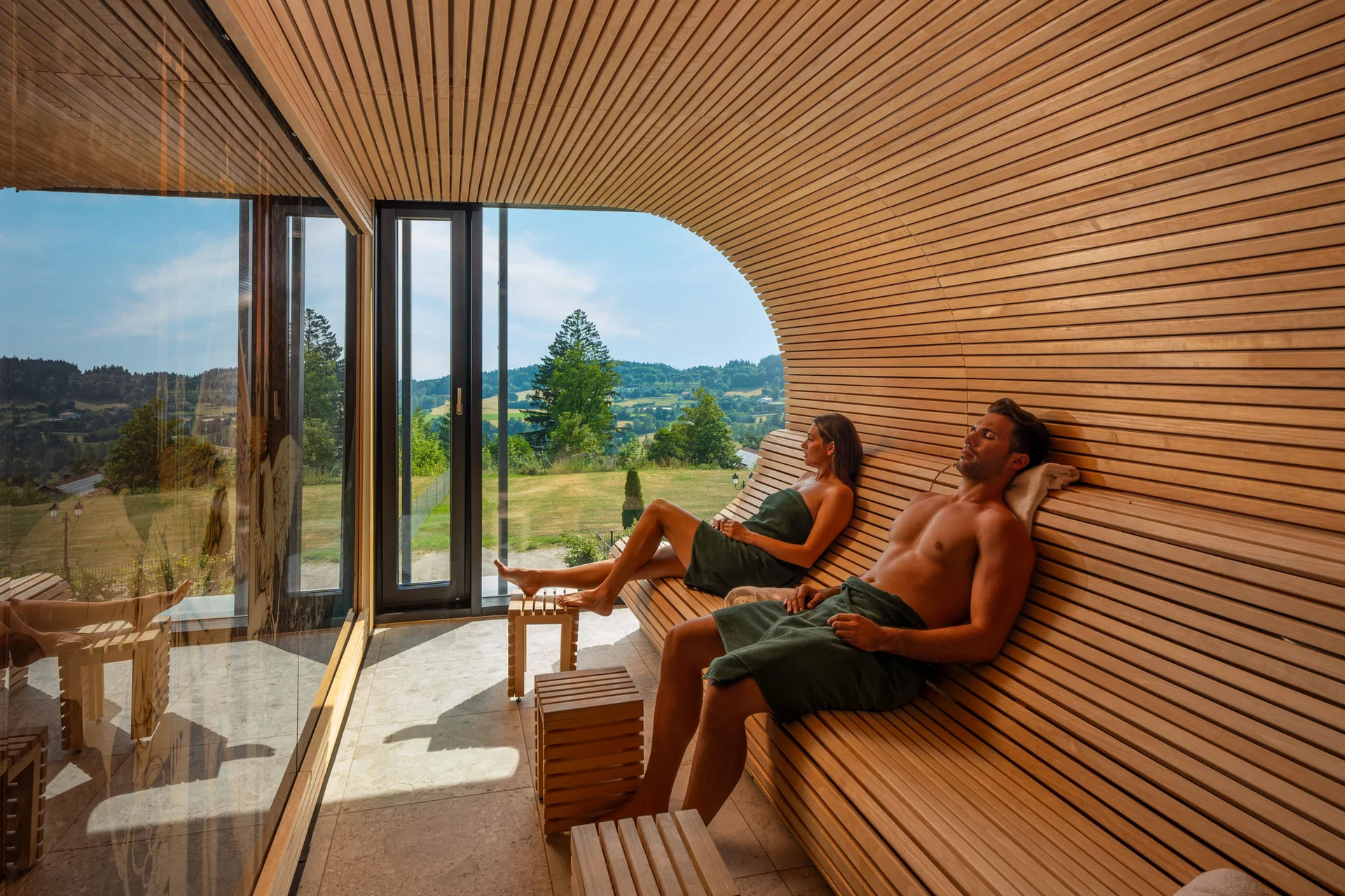 Zwei Personen entspannen in einer Sauna mit Fenster und Blick auf die Landschaft
