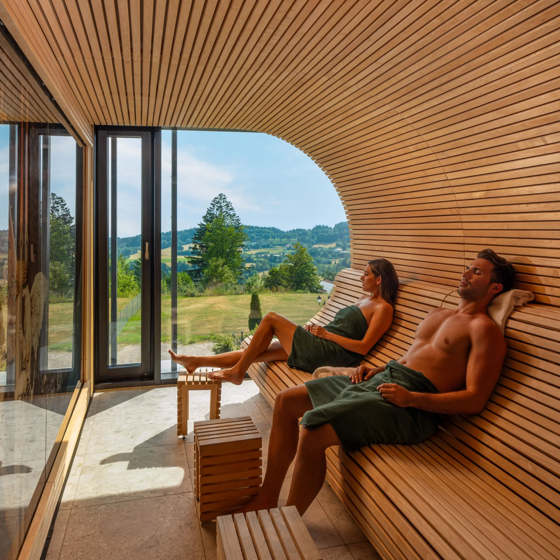 Zwei Personen entspannen in einer Sauna mit Fenster und Blick auf die Landschaft