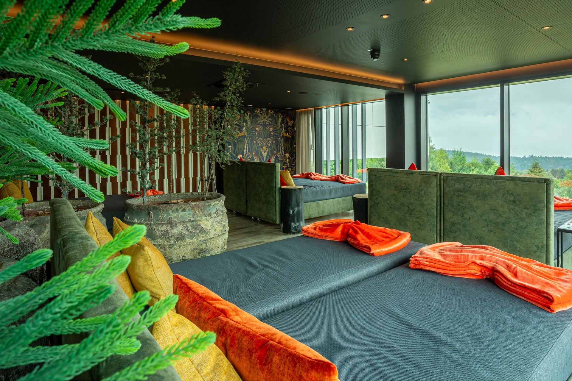 Gemütlicher Aufenthaltsraum mit grünen Sofas, orangen Decken und Panoramafenstern
