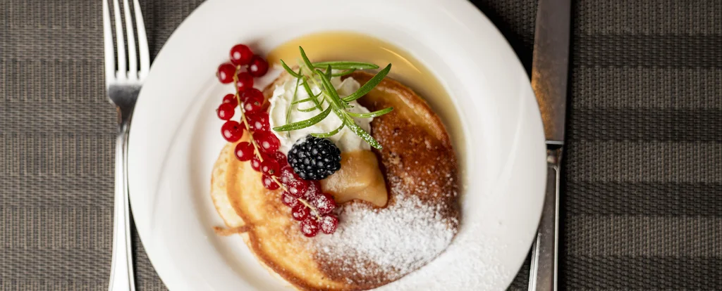 Pfannkuchen mit Beeren, Sahne und Puderzucker auf weißem Teller
