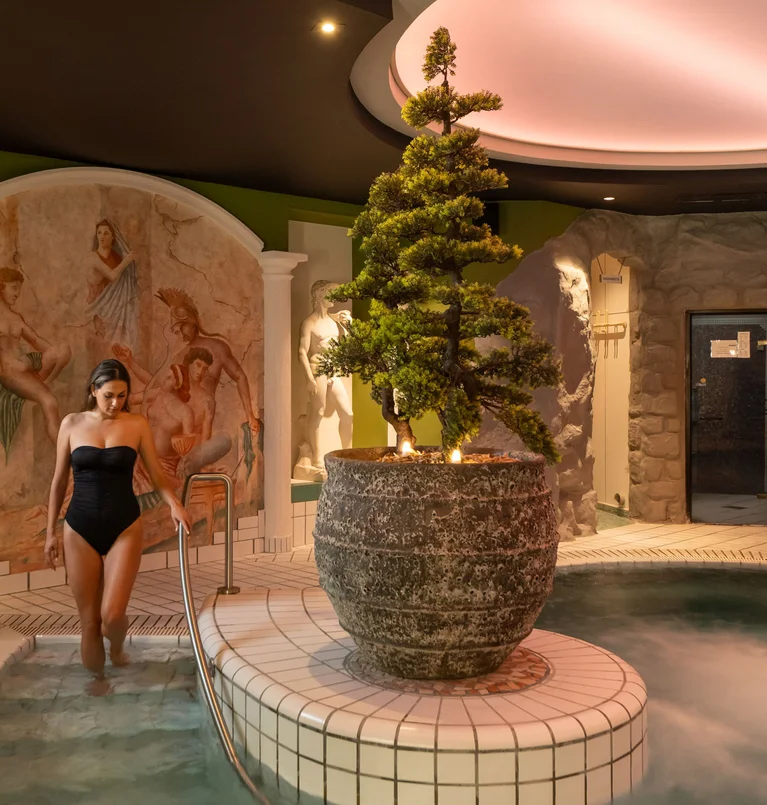 Frau steigt in beheiztes Spa-Becken in einem römisch inspirierten Wellnessbereich
