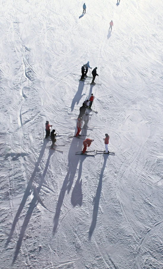 Menschen beim Skifahren auf verschneiter Piste mit langen Schatten