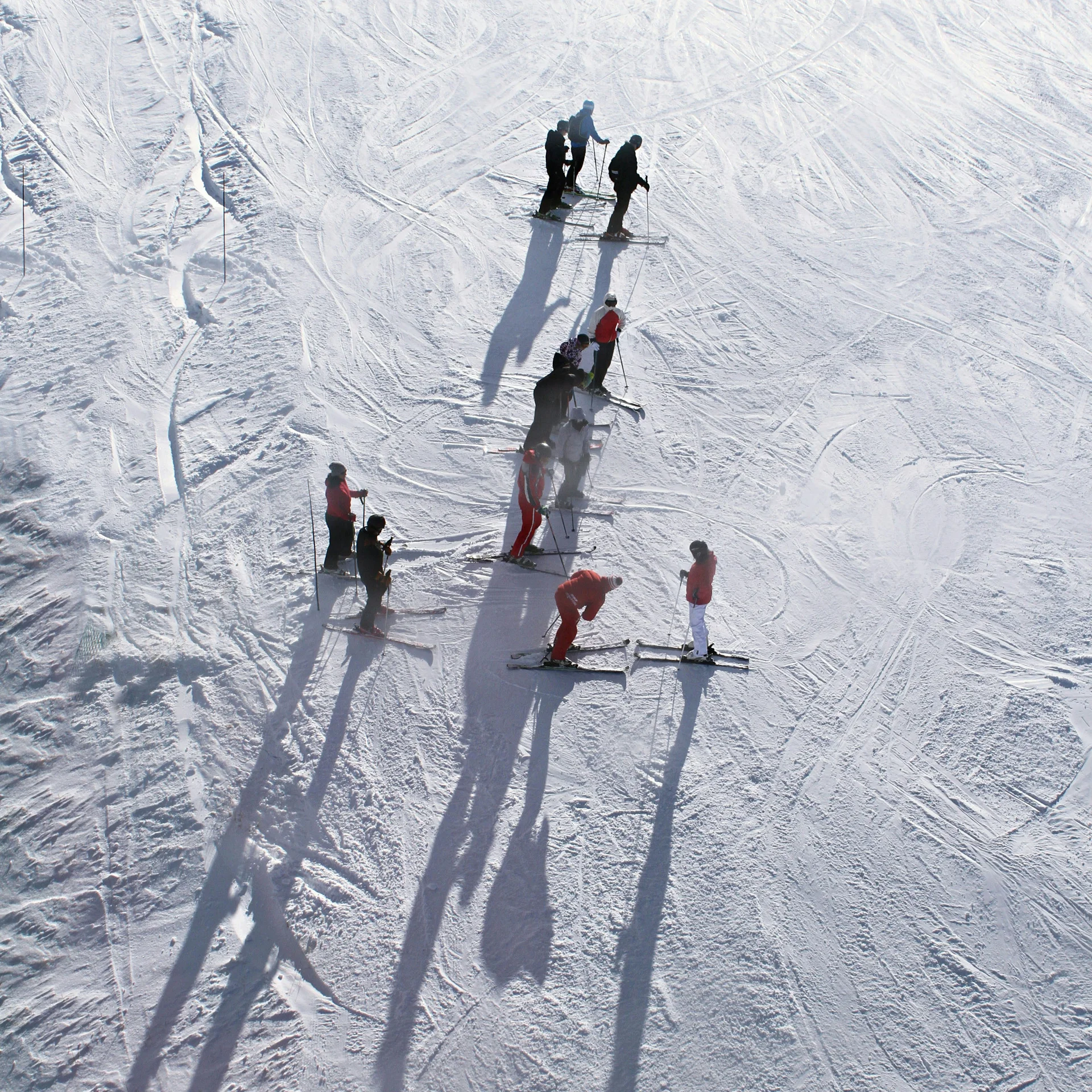 Menschen beim Skifahren auf verschneiter Piste mit langen Schatten