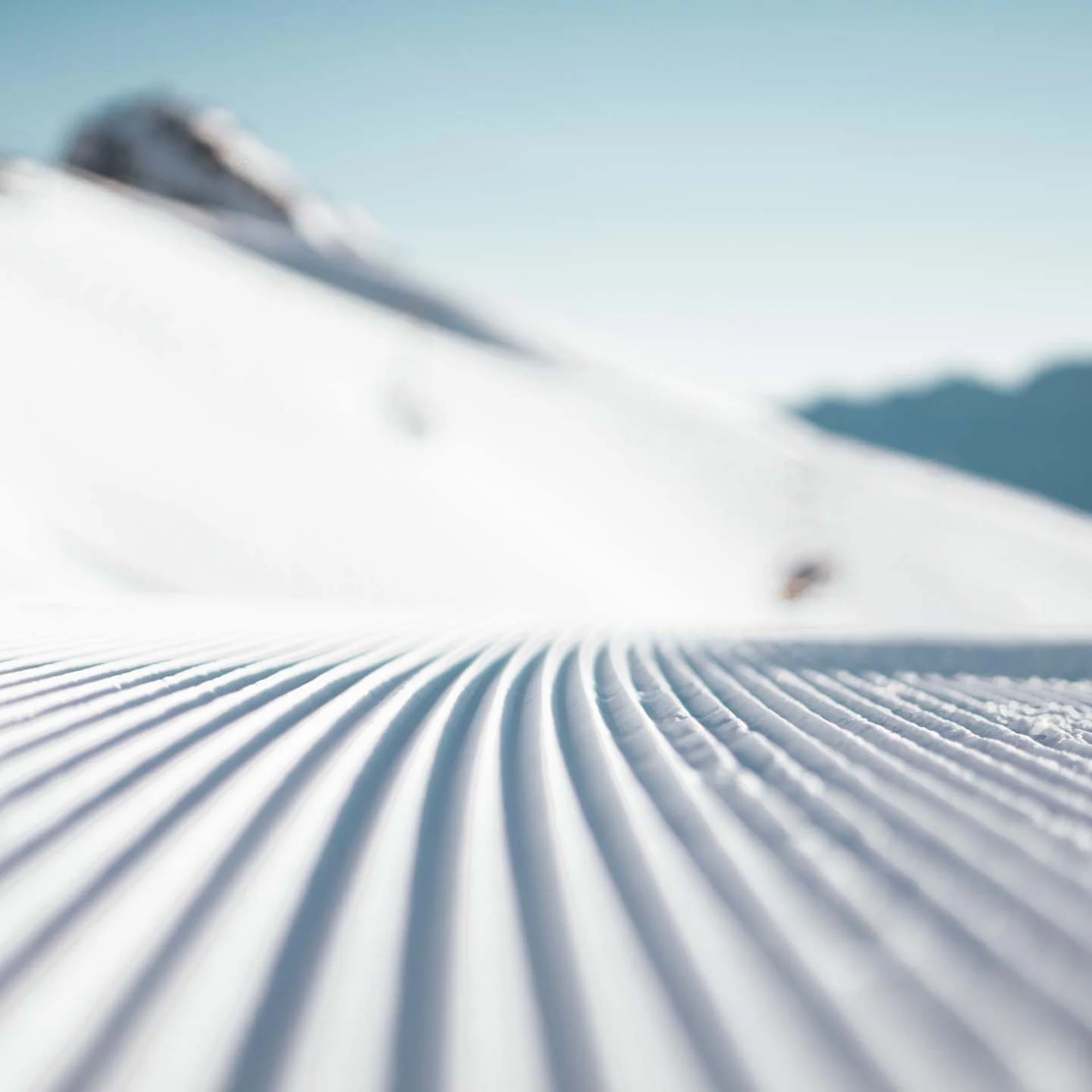 Frisch gespurte Skipiste vor Bergkulisse bei klarem Himmel