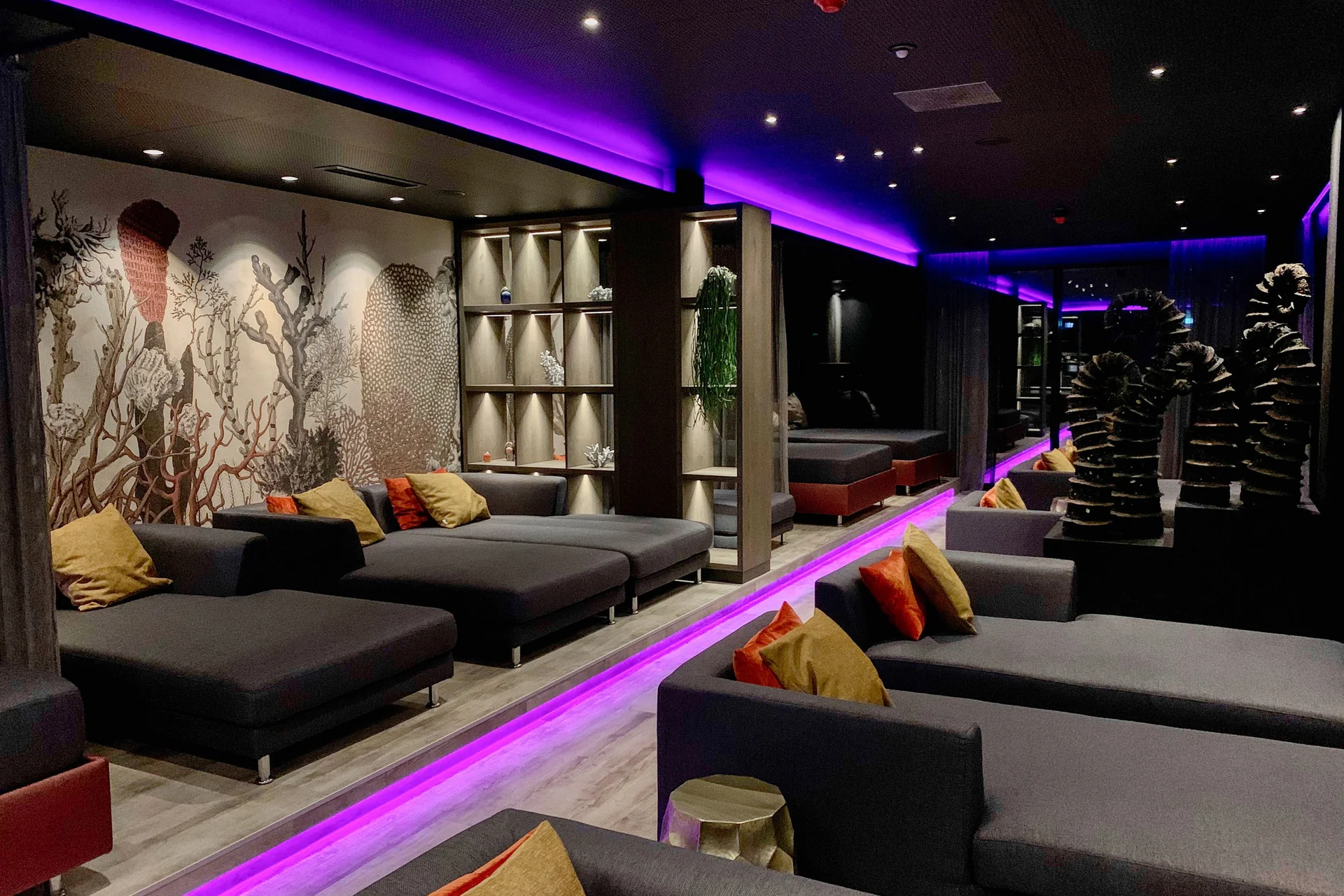 Moderne Lounge mit lila Beleuchtung, grauen Sofas und dekorativer Wandgestaltung