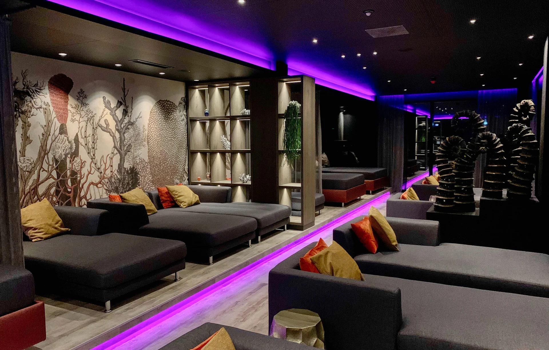 Moderne Lounge mit lila Beleuchtung, grauen Sofas und dekorativer Wandgestaltung