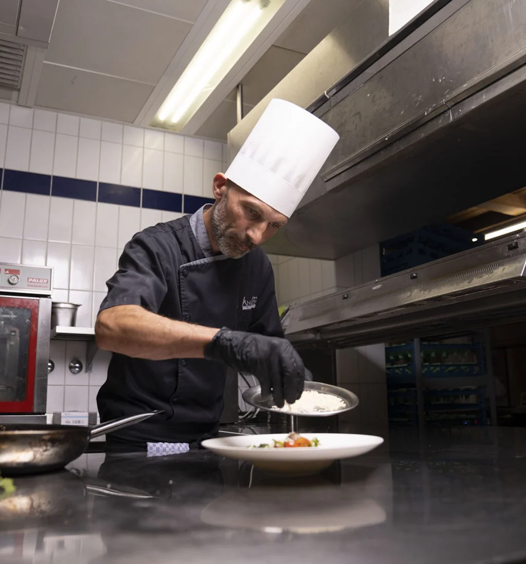 Koch im weißen Hut garniert Gericht in professioneller Restaurantküche